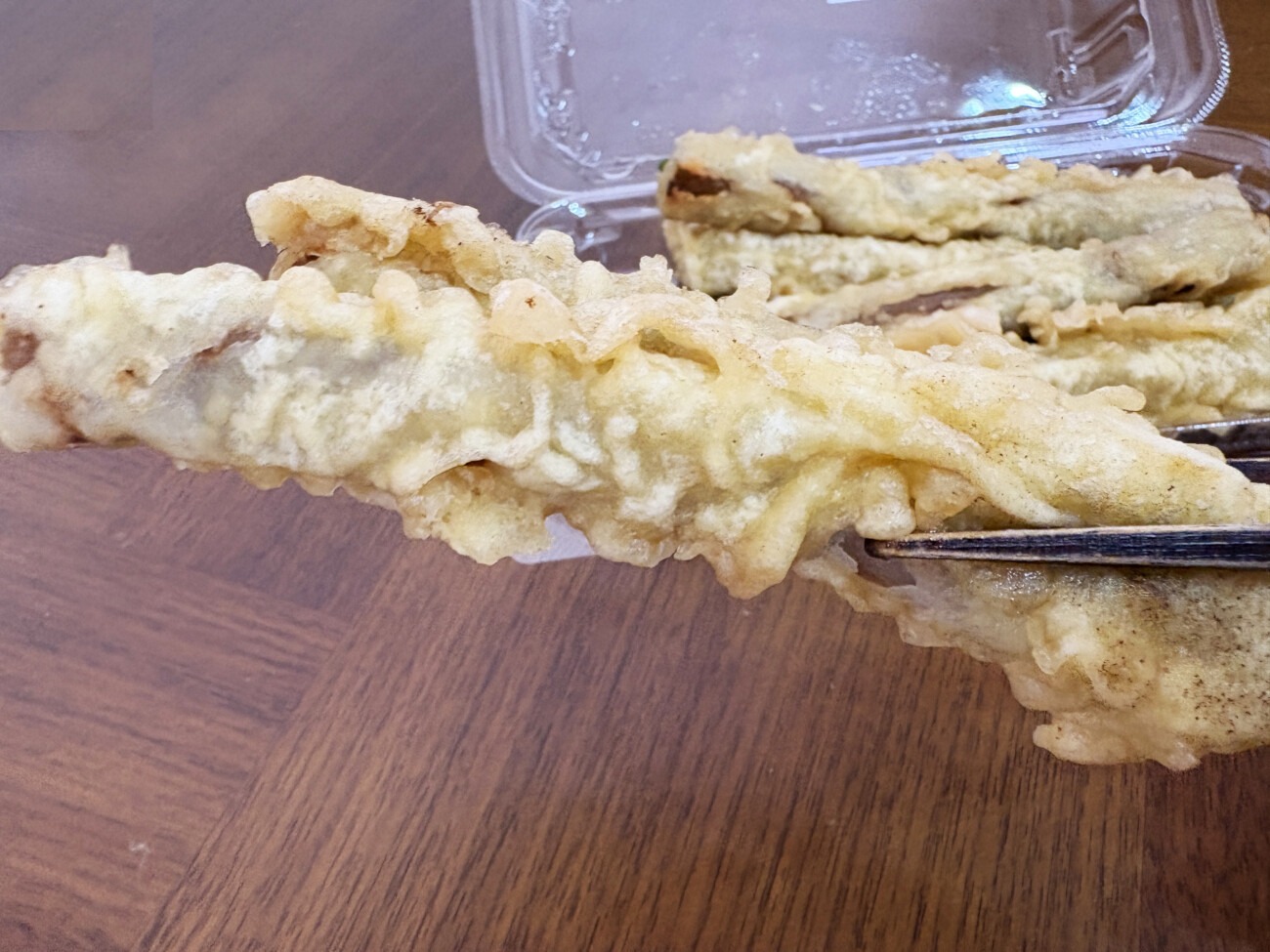 長さのある味付きごぼうの天ぷらを箸で持ち上げたところ