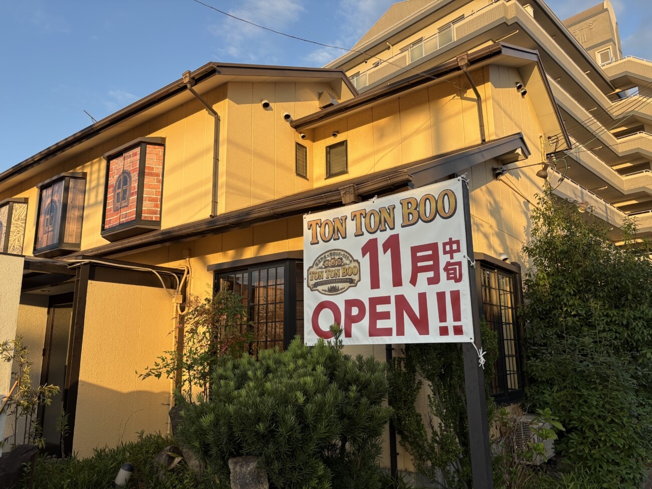 「TON TON BOO 11月中旬OPEN!!」の告知看板と、わら・木・レンガの家を描いた窓